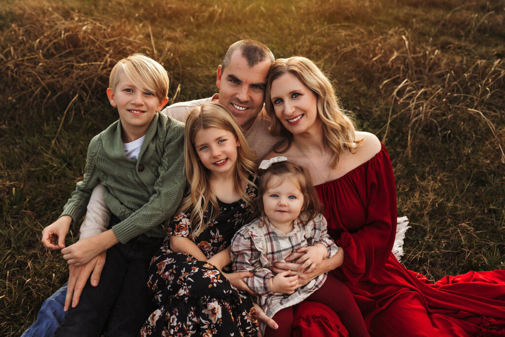 Brittany Moncrieff's family of five, two adults and three kids, smiling on grass with warm autumn sunlight behind.