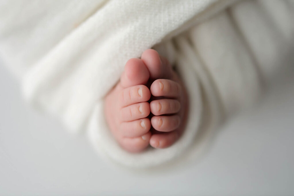 Newborn baby feet wrapped in a soft white blanket, close-up.