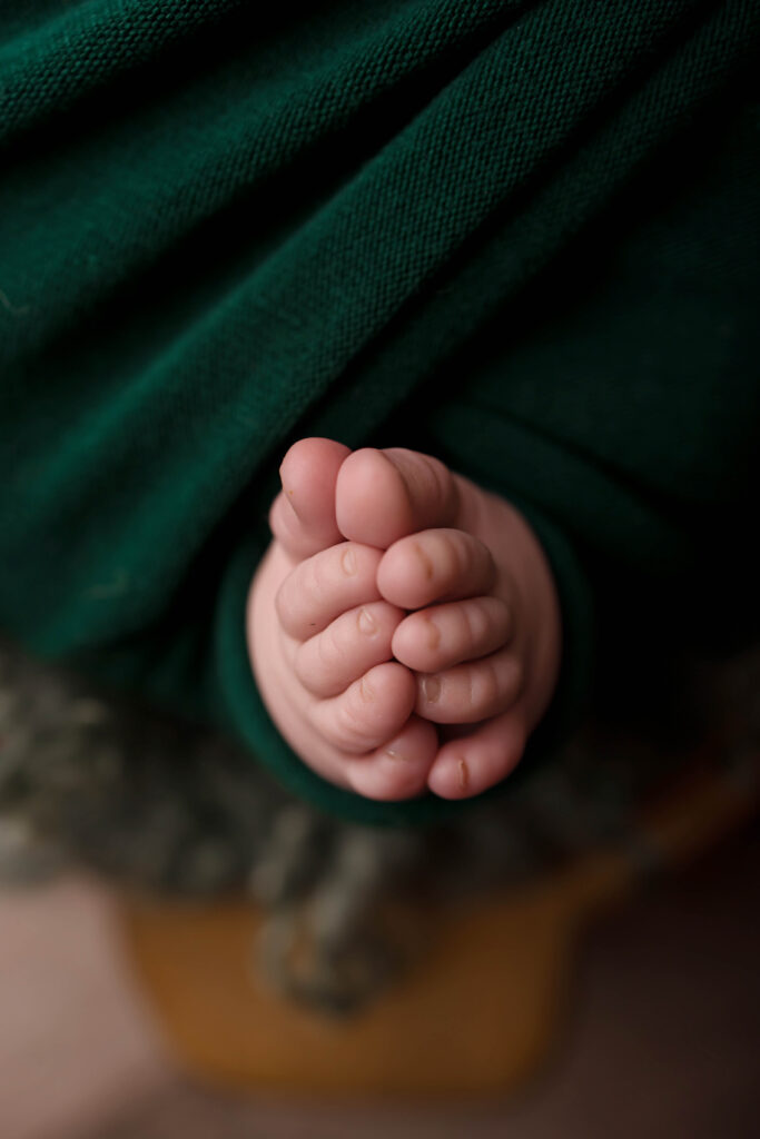 Newborn baby feet wrapped in a dark green blanket, close-up, soft lighting, tender moment.